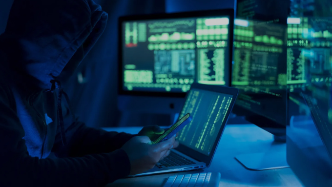 Masked hacker in front of ransomware warning on screen.